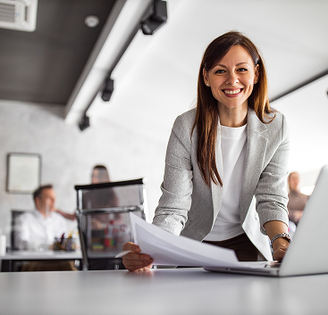 Woman standing at desk with laptop and papers.